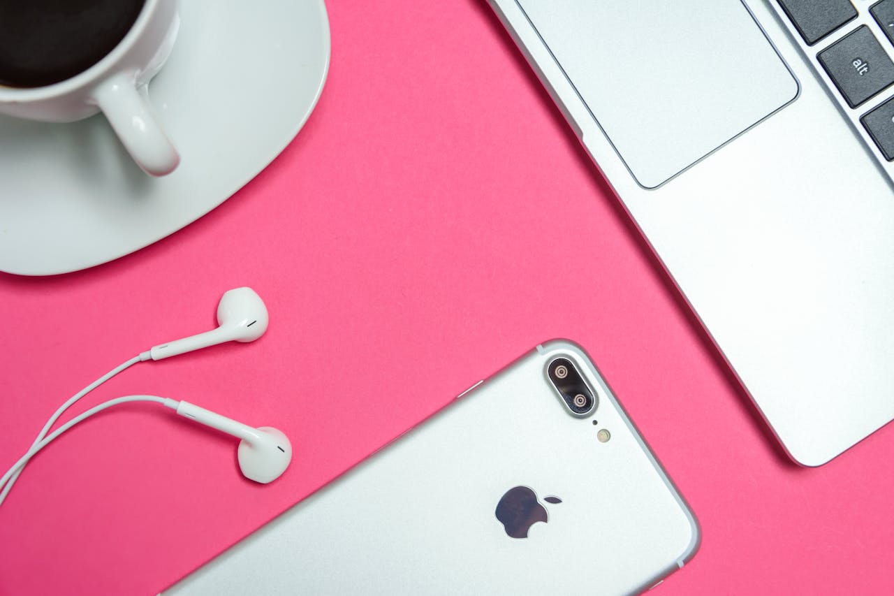 A modern workspace with laptop, smartphone, and coffee cup on a vibrant pink background.